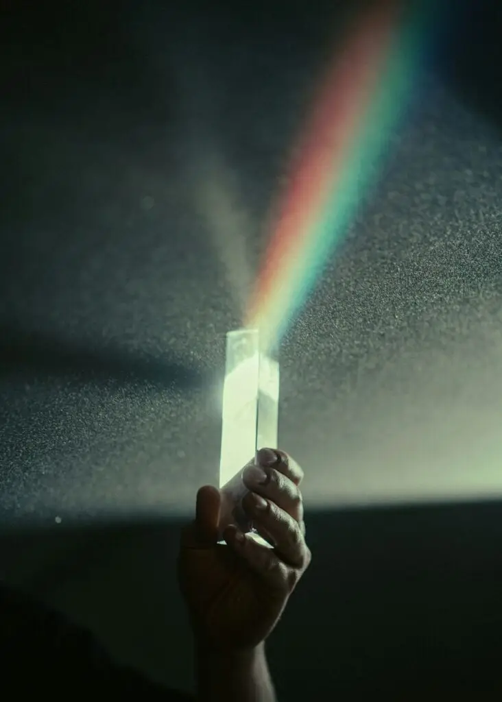 hand holding a crystal prism reflecting light and a rainbow