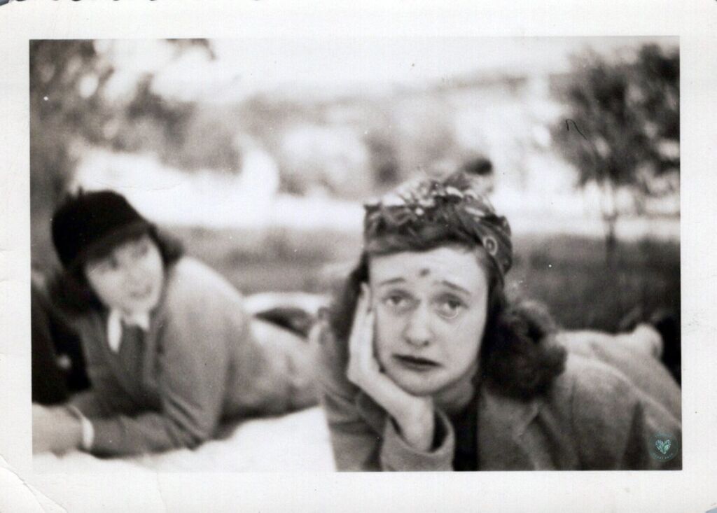 Black and white photo of a woman lying on a picnic blanket with a scraped forehead and nose making a sad face