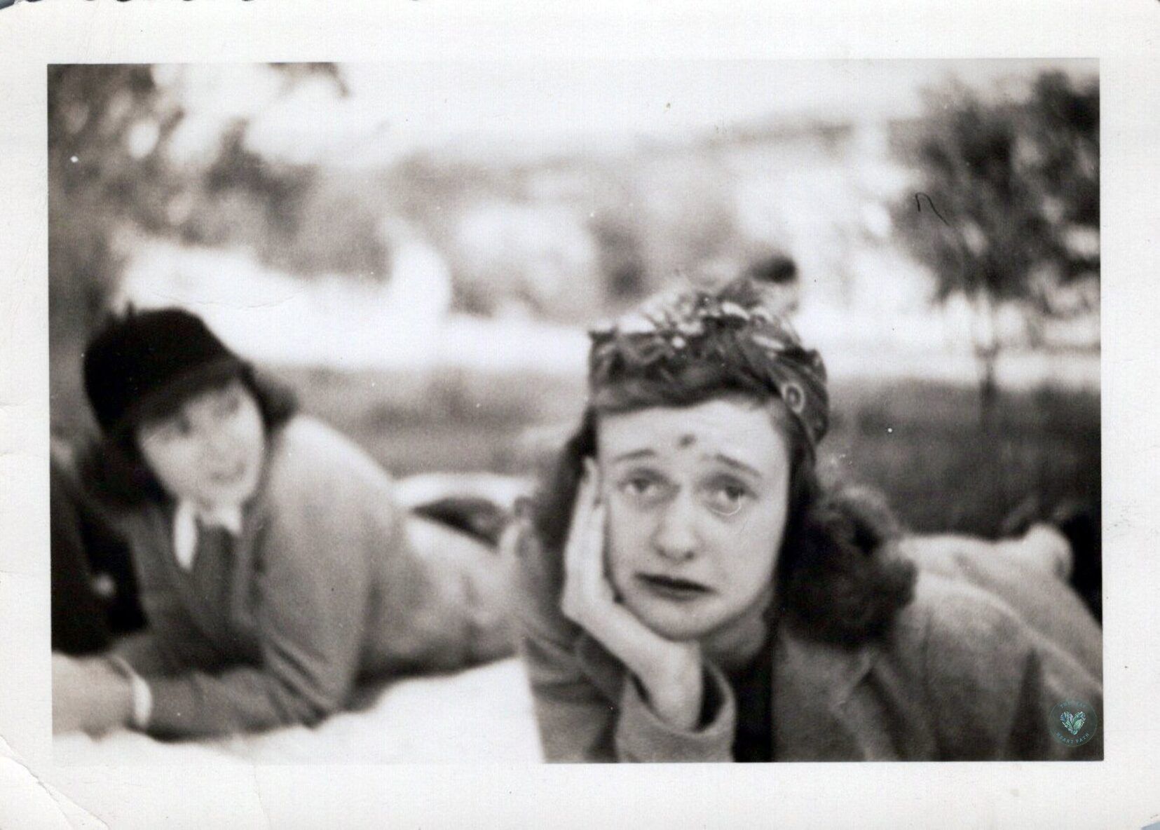 Black and white photo of a woman lying on a picnic blanket with a scraped forehead and nose making a sad face